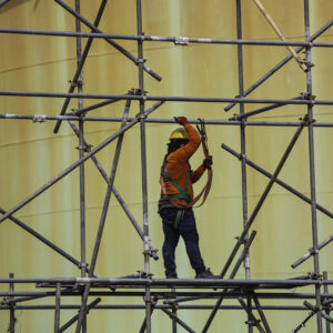 Trabalhador utilizando andaime em obra interna, representando práticas seguras de locação de andaimes.