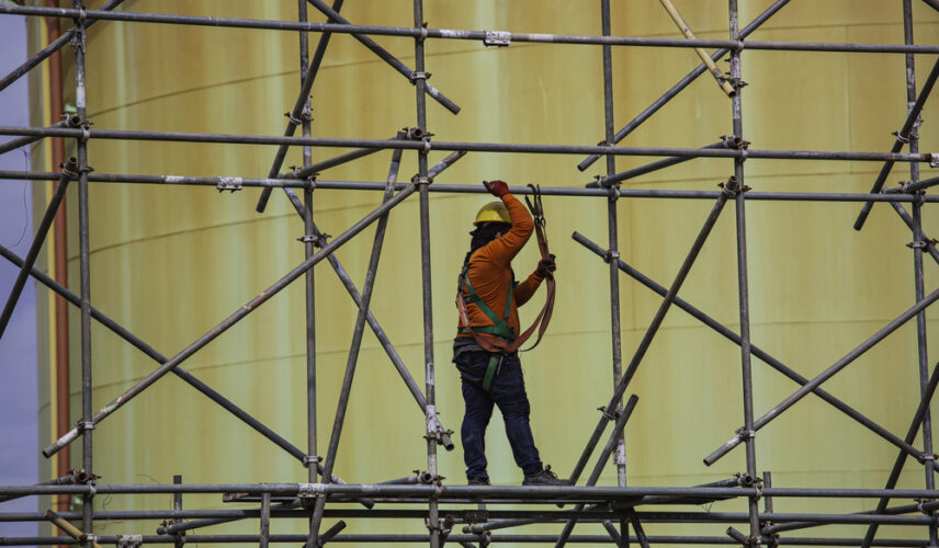 Trabalhador utilizando andaime em obra interna, representando práticas seguras de locação de andaimes.