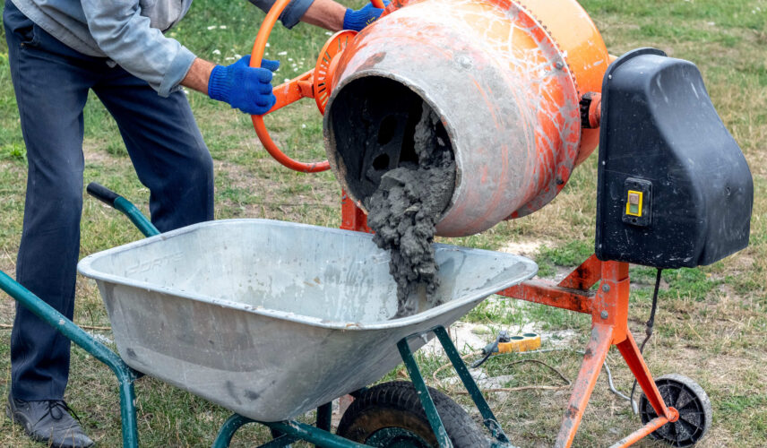Betoneira para obra despejando concreto em carrinho de mão durante preparo no canteiro
