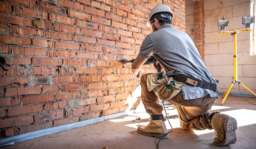 Trabalhador utilizando ferramenta elétrica em obra alimentada por gerador de energia no canteiro